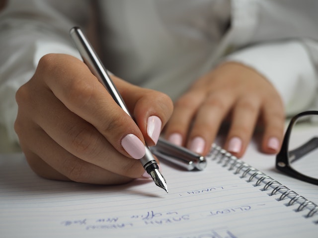 A person holding pen writing in a note book