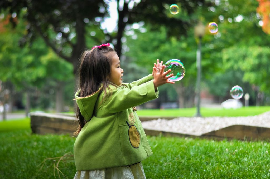 Little girl wearing a green dress playing chasing bubbles outdoors
