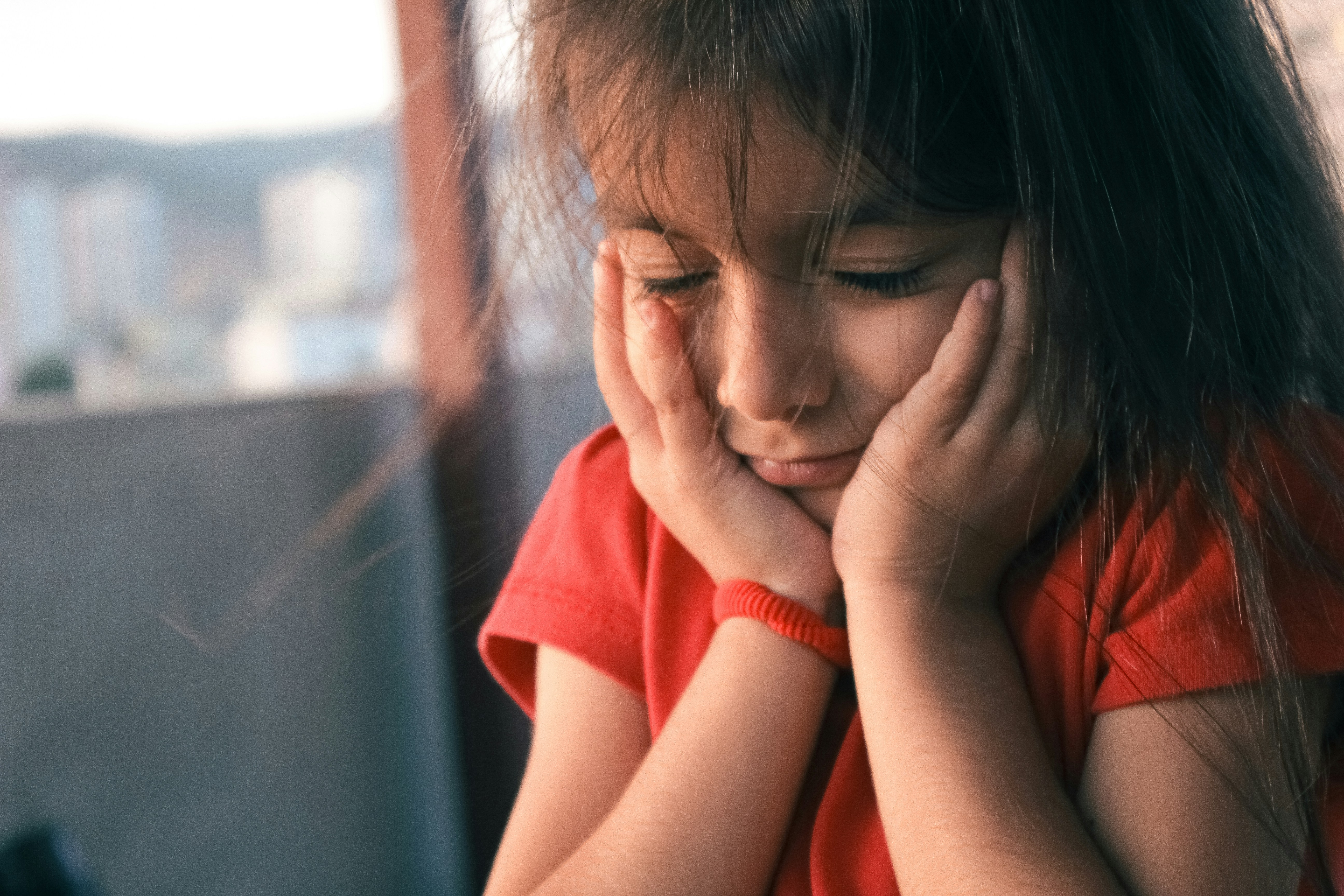 Female child with eyes closed and both hands on her face looking upset and worried